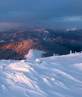 Kış. İnanılmaz fırtınalı bir gökyüzü. Kar beyazı tepeli yüksek dağlar. Karlar altında donmuş ağaçlarla kaplı panoramik bir manzara. Kış. Güzel gökyüzü olan doğal manzara.