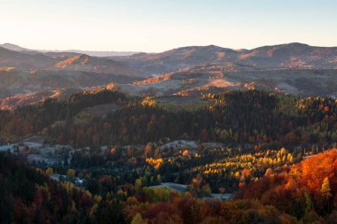Sonbahar kırsal manzarası. Dağlarla, tarlalarla ve sabah karıyla kaplı ormanlarla kaplı bir manzara. Bahçede portakal yapraklarıyla dolu ağaçlar var. Resimli tatil beldesi Karpatyalı, Europa