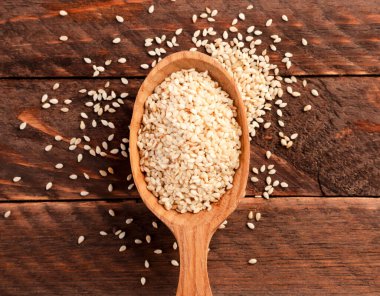 Bir kaşıkta susam tohumu ve ahşap bir arka plana serpilmiş. Üst görünüm