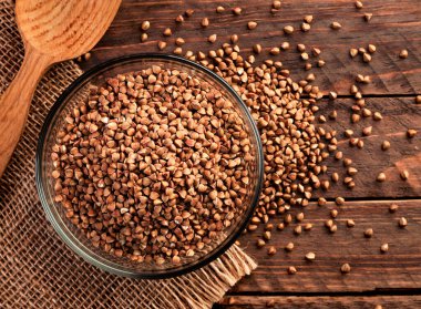 Tahta arka planda yakın plan bir tabakta çiğ kahverengi karabuğday. Yukarıdan görünüm