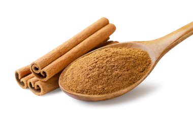 Tahta kaşıkta tarçın tozu ve beyaz arka planda tarçın çubukları. İzole edilmiş