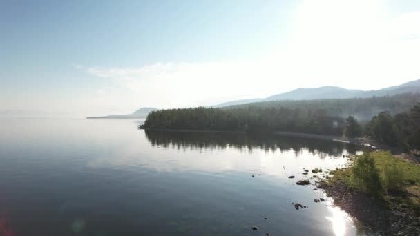 Epische filmische luchtfoto uitzicht Lake Baikal in de ochtend. Turkoois water in een bergmeer met dennenbomen. Uitzicht vanuit de lucht op het blauwe meer en groene bossen. Uitzicht op het meer tussen bergbos. — Stockvideo