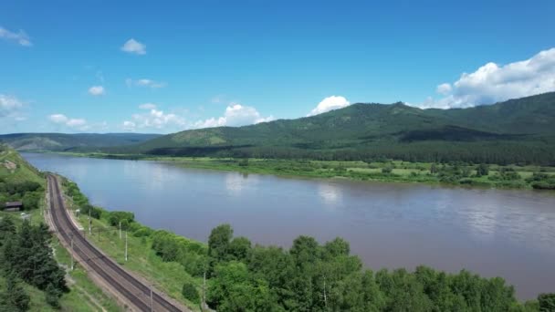 Vliegen boven een gletsjerrivier in Siberië, Rusland met groene bergen en spoorlijn op de achtergrond. — Stockvideo