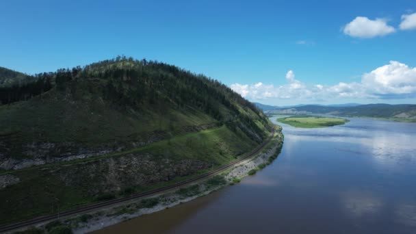 背景に緑の山と鉄道線を持つロシアのシベリアの氷河川の上を飛ぶ. — ストック動画