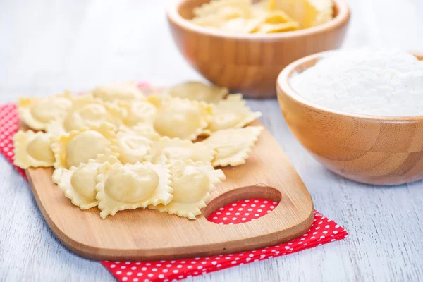 Raw ravioli and flour in bowl — Stock Photo, Image