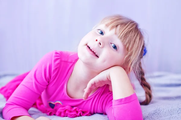 Smiling little girl lying on bed — Stock Photo, Image