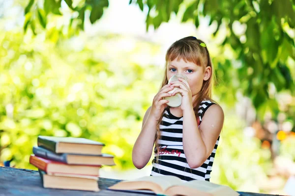 Flicka konsumtionsmjölk med böcker. — Stockfoto