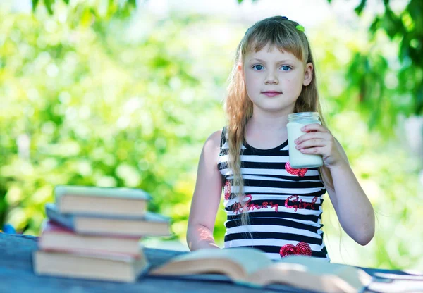 Flicka konsumtionsmjölk med böcker. — Stockfoto
