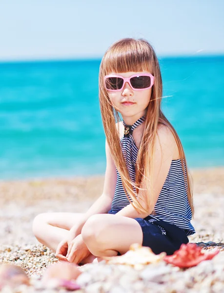 Klein meisje in zonnebril op het strand — Stockfoto