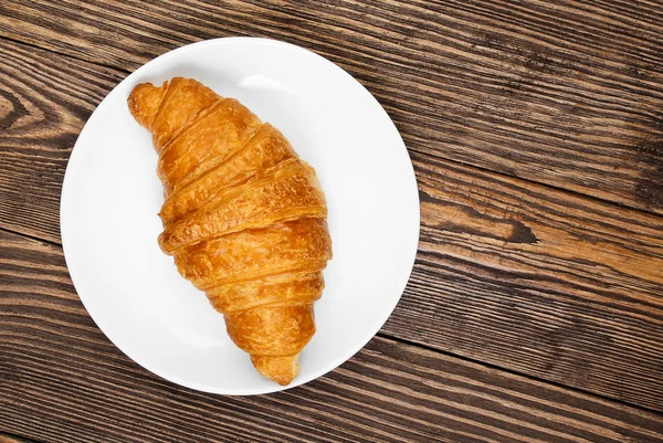 Croissant auf einem Teller auf einem alten Holztisch. — Stockfoto