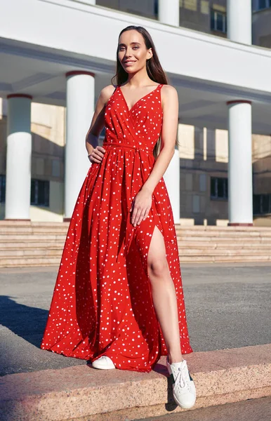 Street fashion: beautiful sweet girl in red dress and sneakers. Portrait of alluring smiling young woman