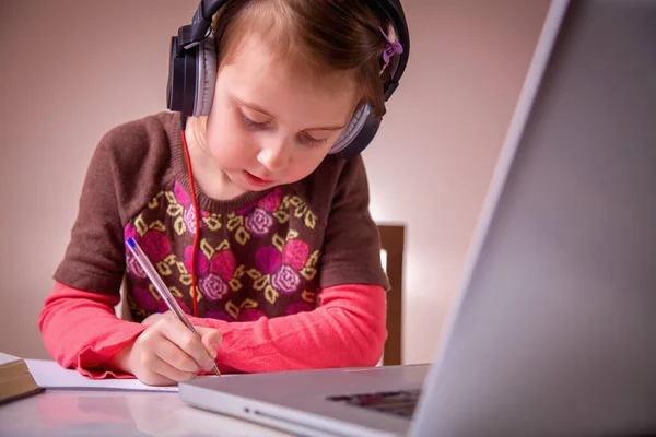 Distance education. Serious young girl learning remotely with headphones and laptop.