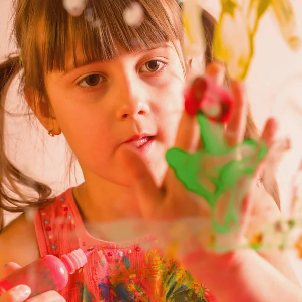 Portrait of beautiful young girl painting painting artwork on glass with colorful hands and finger. Happy childhood, art, painting lessons concept. Selective focus on finger.