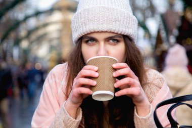 Winter holidays, christmas, hot drinks and people concept. Happy beautiful young woman tourist in warm clothes drinking coffee from disposable paper cups in old town
