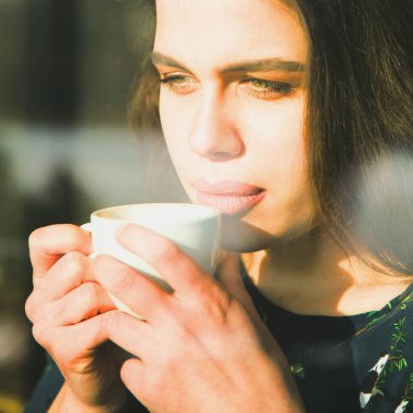 Kahve fincanı olan güzel bir kadın. Bir pencerenin arkasını göster. 