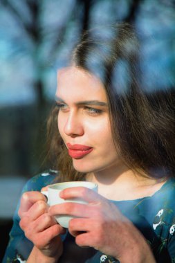 Winter holidays, christmas, hot drinks concept. Happy beautiful young woman drinking coffee behind a window. Vertical image. 