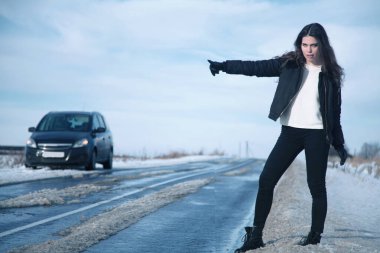 Kış yolundaki bozuk araba. Arabayı durdurmaya çalışan genç ve güzel bir kadın. Dikey resim.