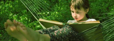 Genç kız rahat hamakta yeşil çimlere karşı kitap okuyor. Güzel bayan çocuk bahçede dinleniyor. Yatay resim.