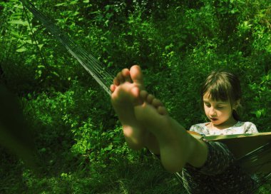 Genç, güzel bir kız, hamakta kitap okumaktan zevk alıyor. Dışarıda, güneşin altında yeşil bahçede. Tasarım için alanı kopyala.