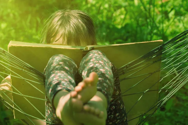 Genç kız rahat bir hamakta yeşil çimlere karşı kitap okuyor.