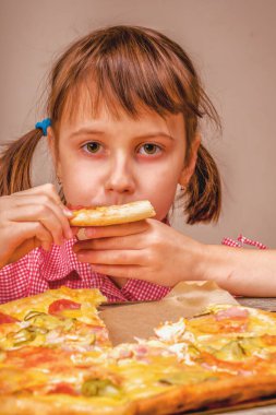 Genç ve çekici bir kızın yakın portresi lezzetli bir dilim pizzayı seviyor, bu tadı seviyor, iştahı yerinde. Kapalı alanda aç bir kadın çocuk. Boş kopyalama alanı.