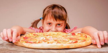 Genç ve çekici bir kız lezzetli pizzayı seviyor, bu tadı seviyor, iştahı yerinde. Kapalı alanda aç bir kadın çocuğunun komik görüntüsü. Yatay resim.