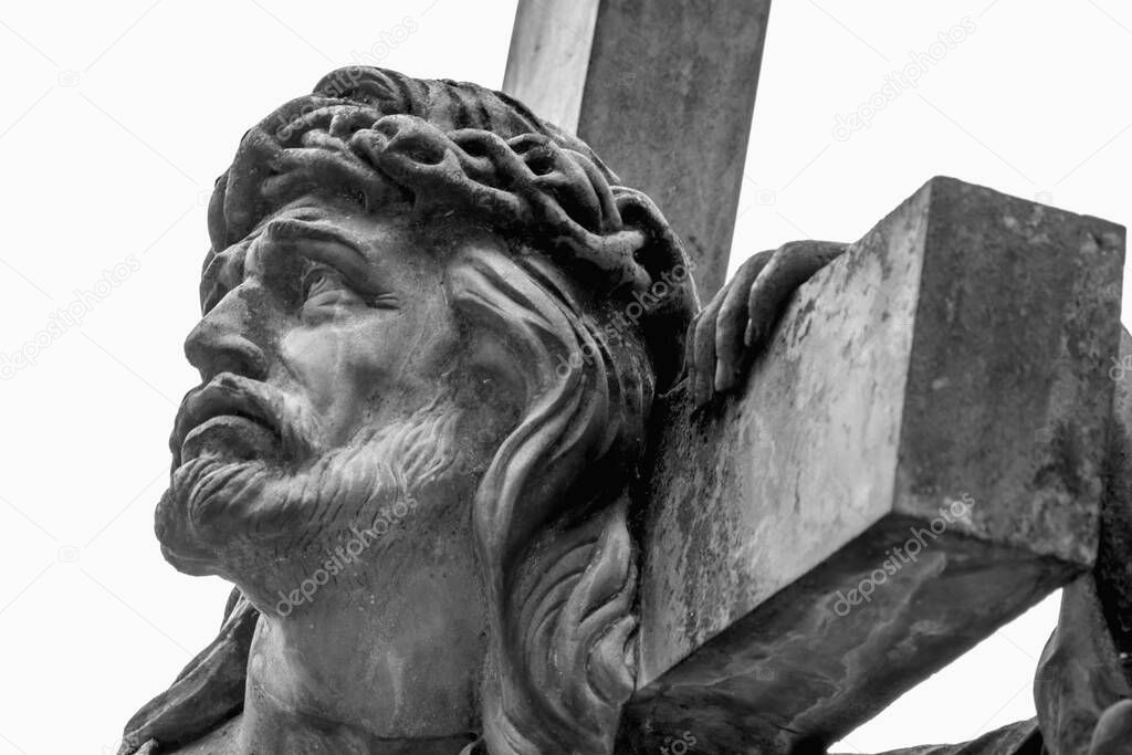 Close up an ancient statue of Jesus Christ with cross. Selective focus on eyes. Free copy space. Horizontal image