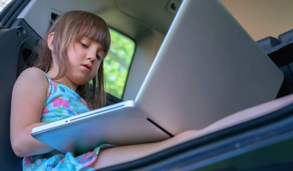 Learn lways and everywhere. Young beautiful child girl sitting in the car and using laptop.
