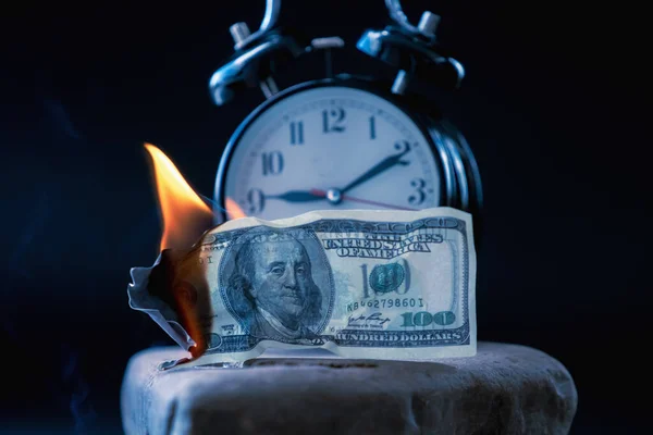 Burning US Dollar bills and the clock as symbol of lost time and opportunities. Selective focus on money. Horizontal image.