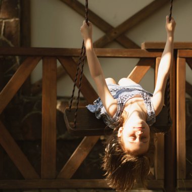 Güzel genç kız salıncakta baş aşağı oturuyor. Yaz tatili ve mutlu çocukluk konsepti. 