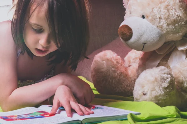 little child girl reading a magic book with a toy teddy bear