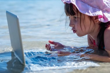 Ofis kavramında yaz sıcağı. Genç ve güzel bir kız serbest çalışıyor. Denizin sıcağından kaçıyor ve tatillerde internet defteriyle birlikte serin sularda çalışıyor. Yatay resim.