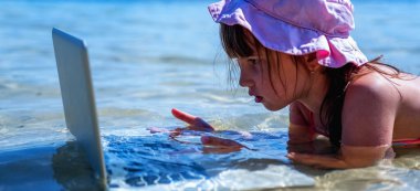 Ofis kavramında yaz sıcağı. Genç ve güzel bir kız serbest çalışıyor. Denizin sıcağından kaçıyor ve serin sularda netbook ile uzaktan çalışıyor. Yatay resim.