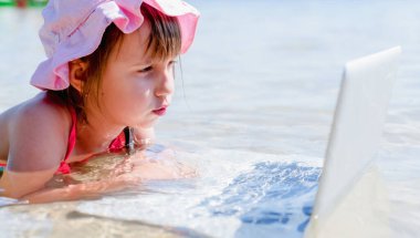 Kavramsal görüntü: Bu yaz çalışanları ofisten nasıl çıkaracağız. Genç iş kızı deniz suyunda netbook ile uzaktan yakından çalışıyor.. 