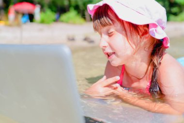 Dizüstü bilgisayarla çalışan ve sahilde buluşan genç iş kadınının komik portresi. Konsept: serbest çalışma, tatiller, mesafe çalışması, sosyal mesafeler, e-öğrenme. Yatay resim.