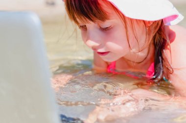 Kumsalda dizüstü bilgisayar kullanan genç bir iş kızı. Konsept: serbest çalışma, tatiller, mesafe çalışması, sosyal uzaklık, e-öğrenme, çevrimiçi buluşma.