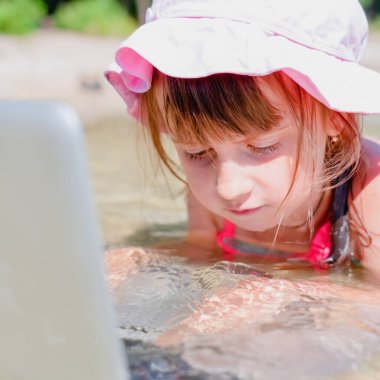 Kumsalda dizüstü bilgisayar kullanan genç bir iş kızı. Konsept: serbest çalışma, tatiller, mesafe çalışması, sosyal uzaklık, e-öğrenme, yaratıcı meslek, çevrimiçi buluşma.