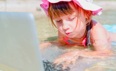 Kumsalda dizüstü bilgisayar kullanan genç ve güzel bir kız. Konsept: serbest çalışma, tatiller, mesafe çalışması, sosyal uzaklık, e-öğrenme, yaratıcı meslek, çevrimiçi buluşma.