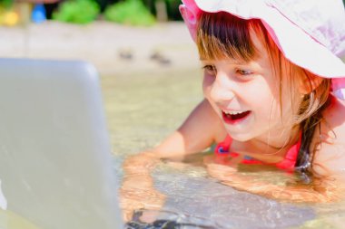 Her zaman ve her yerde öğrenme kavramı. Mutlu genç kız dışarıda tropikal denizde bilgisayarla uzaktan öğreniyor..