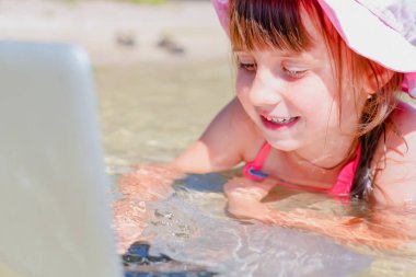 Kumsalda dizüstü bilgisayar kullanan genç ve güzel bir kız. Serbest çalışma, tatiller, mesafeli çalışma, sosyal uzaklık, yaratıcı profesyonellik, online konsept buluşması.