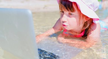 Kumsalda dizüstü bilgisayar kullanan genç ve güzel bir kız. Serbest çalışma, tatiller, mesafeli çalışma, sosyal mesafeler, e-öğrenme, yaratıcı profesyoneller, online konseptle tanışma. Yatay resim.