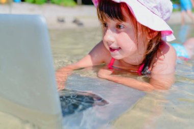 Kumsalda dizüstü bilgisayar kullanan genç ve güzel bir kız. Serbest çalışma, tatiller, mesafeli çalışma, sosyal uzaklık, e-öğrenme, yaratıcı profesyonellik, online konseptle buluşma