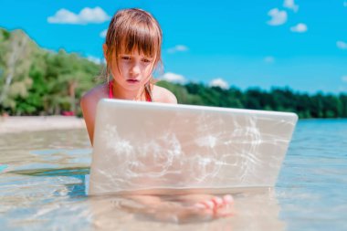 Aynı anda hem çalış hem dinlen. Uzaktan kumandalı güzel bir genç, tropikal deniz suyunda dışarıda dizüstü bilgisayarla öğreniyor. Yatay resim.