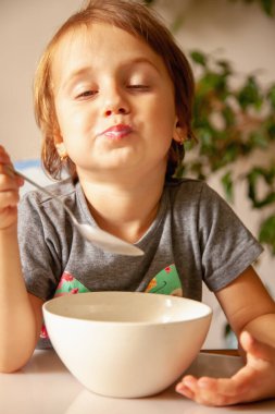 Çocuk maması konsepti. Mutlu, güzel bir kızın komik portresi gülüyor ve kahvaltı yapıyor.. 