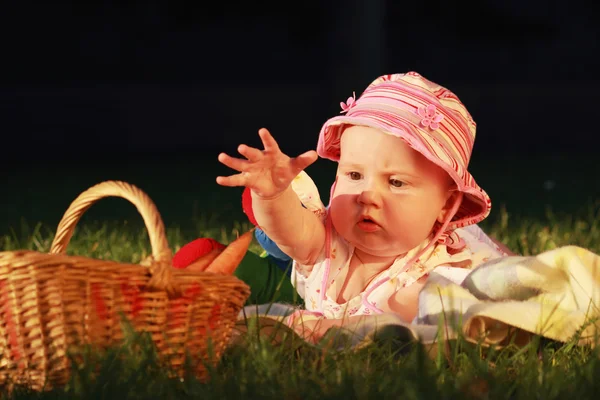 Beautiful baby girl looks in basket with vegetables — Stock Photo, Image