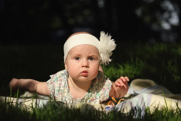 Adorable baby girl lying on green summer lawn — Stock Photo, Image