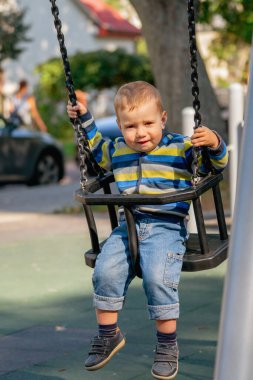Kavramsal görüntü: Mutlu çocukluk. Gülümseyen bir çocuk salıncak zincirlerine sıkıca tutunur. Dikey resim.
