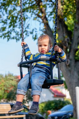 Kavramsal görüntü: Mutlu çocukluk. Gülümseyen bir çocuk salıncakta sallanmaktan hoşlanır. Dikey resim.