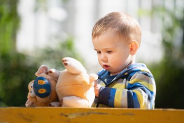 Kavramsal görüntü: Mutlu çocukluk. Küçük bir çocuk oyuncak arkadaşıyla dışarıda oynuyor..
