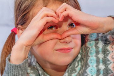 Güzel genç kız aşkın sembolü olarak parmaklarıyla kalp hareketi yapıyor.